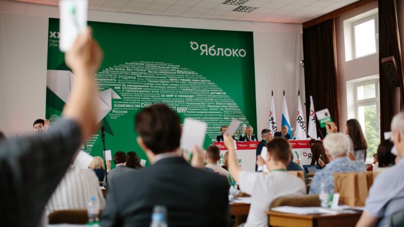 Delegați votând la congresul partidului Iabloko, în fața unui panou cu sigla partidului