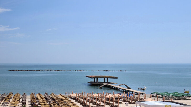 Plaja din Mamaia văzută de sus, cu rânduri de umbrele și șezlonguri și un ponton în mare